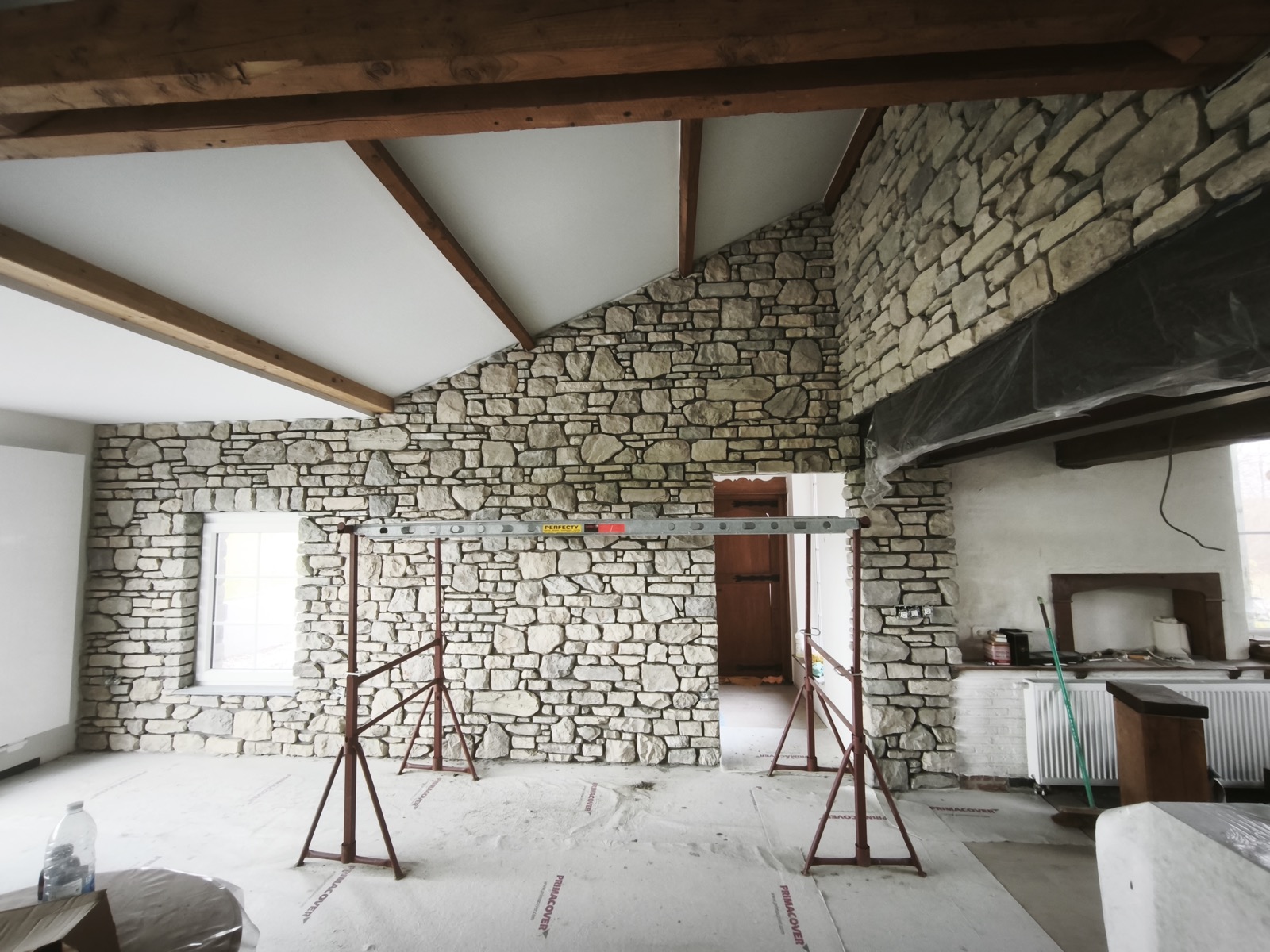 Chantier de pose de pierre reconstituée en intérieur, mur de salon avec poutres apparentes
